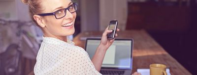 Gründe, warum Fotos bei ElitePartner nicht sichtbar sind werden durch Frau die gerade mit Handy am Laptop über Ihre Schulter schaut dargestellt