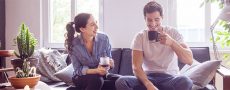 Ein Paar trinkt zu Hause einen Kaffee, er schaut unsicher zu Boden