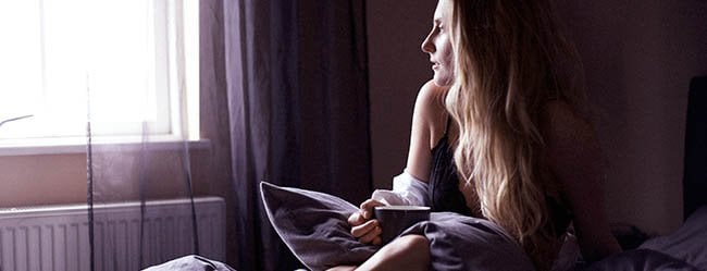 Frau sitzt verzweifelt im Bett und blickt aus dem Fenster um herauszufinden wie sie Trennung verarbeiten kann