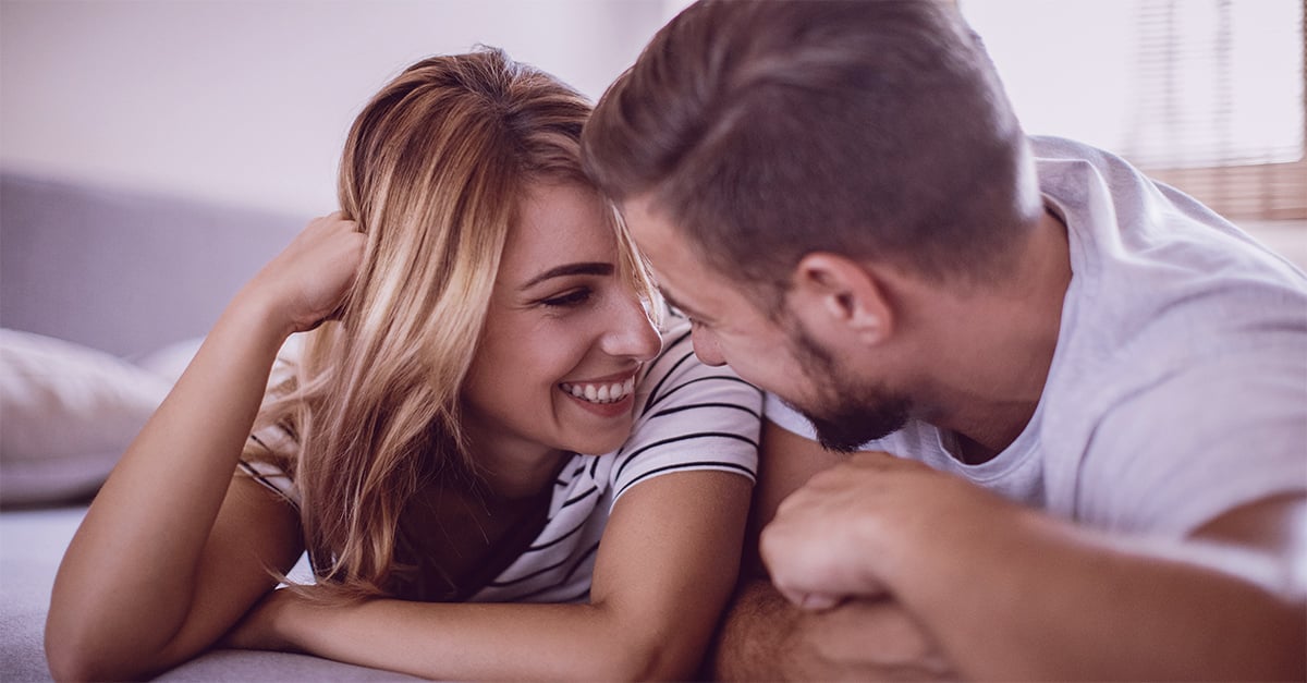 Mann und Frau in einer Rebound-Beziehung liegen auf dem Bauch und lächeln sich an.