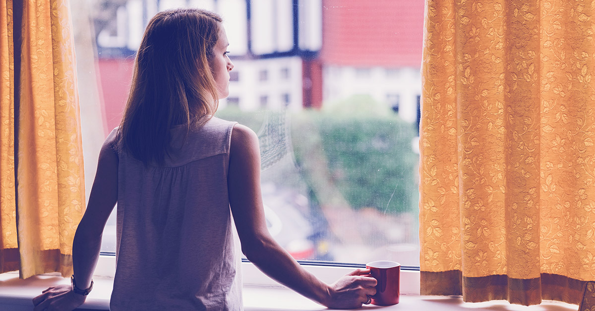 Frau schaut aus dem Fenster als Symbol für emotionale Abhängigkeit